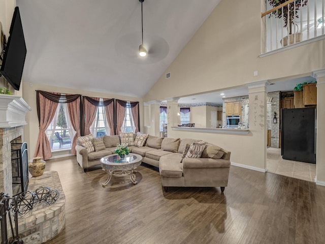 living area with a fireplace, visible vents, light wood-style floors, high vaulted ceiling, and ornate columns