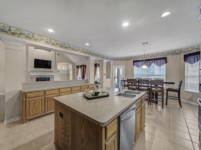 kitchen featuring dishwasher, a brick fireplace, light tile patterned floors, an island with sink, and decorative light fixtures