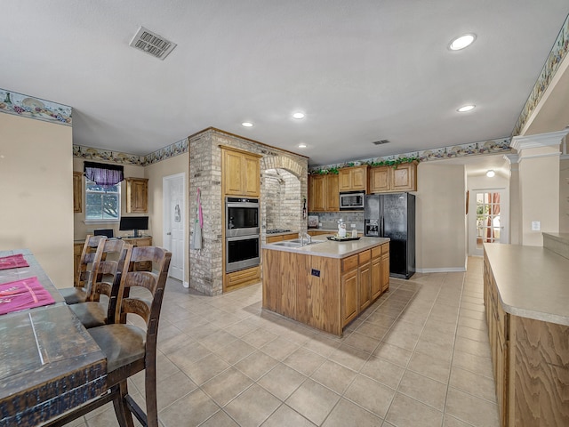 kitchen featuring backsplash, decorative columns, stainless steel appliances, a center island, and light tile patterned flooring