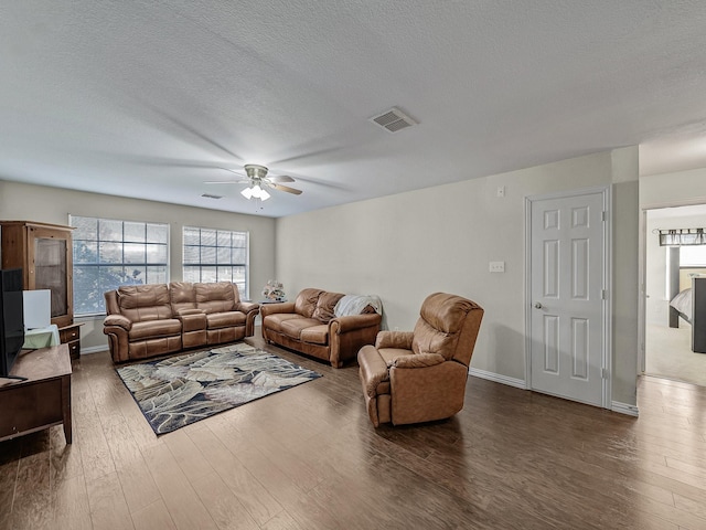 living area with a textured ceiling, wood finished floors, visible vents, baseboards, and a ceiling fan