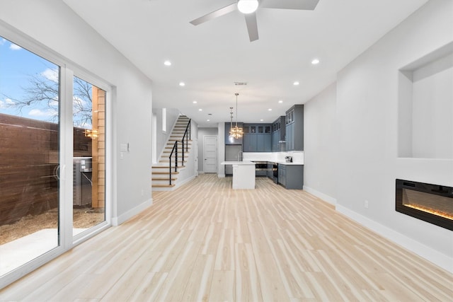 unfurnished living room featuring ceiling fan with notable chandelier and light hardwood / wood-style floors