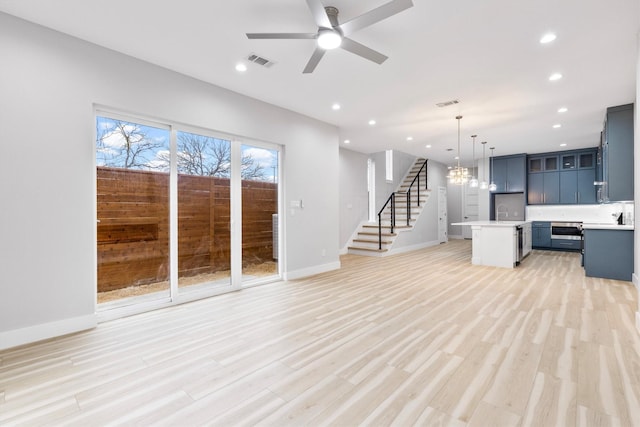 unfurnished living room featuring ceiling fan with notable chandelier and light wood-type flooring