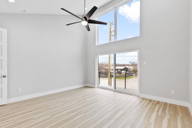 unfurnished living room featuring a towering ceiling, ceiling fan, and light wood-type flooring