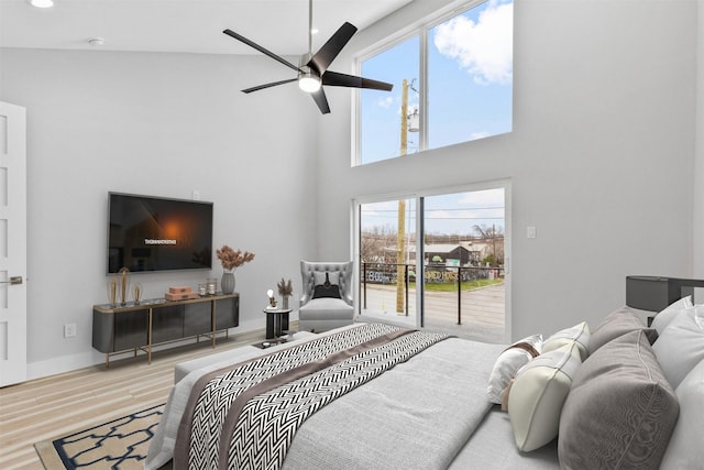 bedroom featuring ceiling fan, a towering ceiling, access to exterior, and light hardwood / wood-style floors