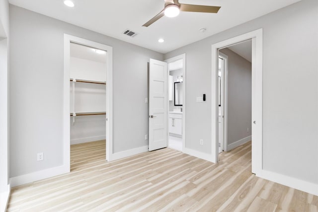 unfurnished bedroom featuring ensuite bathroom, a walk in closet, ceiling fan, light wood-type flooring, and a closet