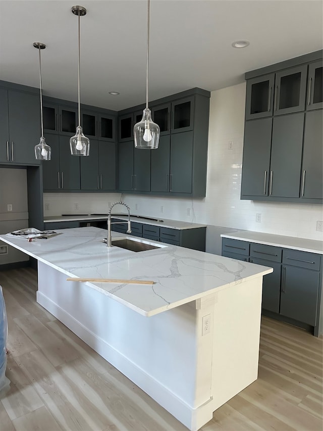 kitchen with sink, light hardwood / wood-style flooring, light stone countertops, and an island with sink