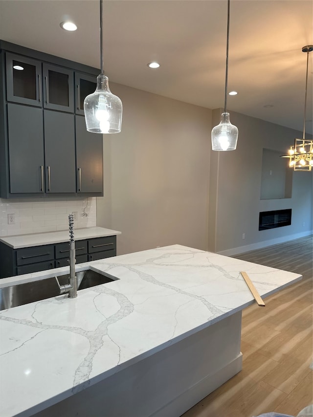 kitchen featuring sink, tasteful backsplash, hanging light fixtures, light stone countertops, and light hardwood / wood-style floors