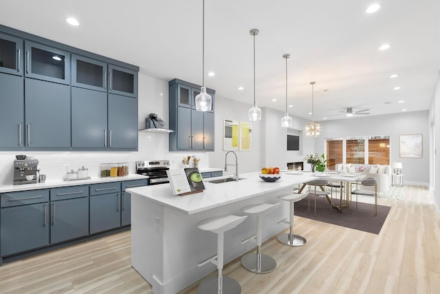 kitchen featuring stainless steel range with electric cooktop, sink, blue cabinetry, and an island with sink