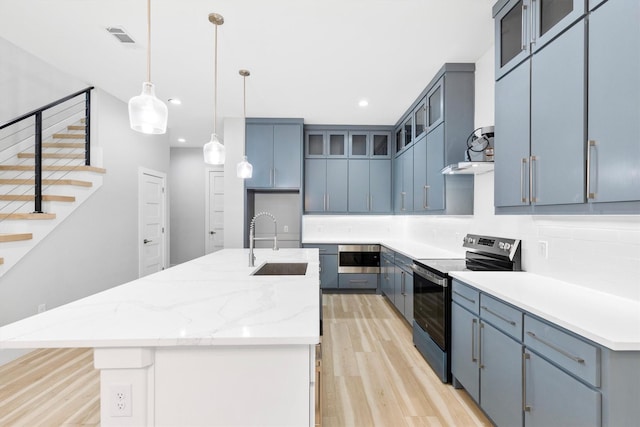 kitchen featuring sink, stainless steel electric range, blue cabinetry, and a center island with sink