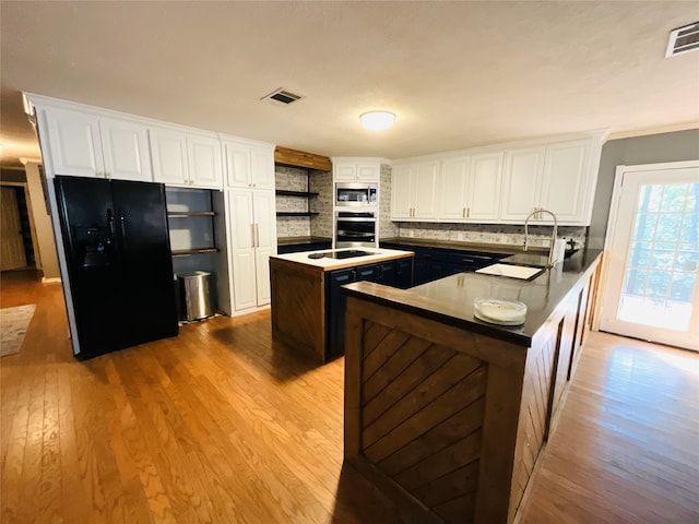 kitchen featuring white cabinetry, sink, backsplash, a kitchen island with sink, and black appliances