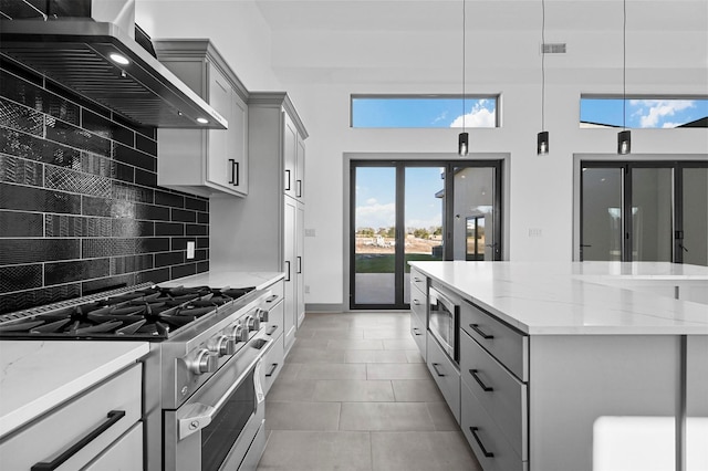 kitchen featuring appliances with stainless steel finishes, backsplash, gray cabinetry, wall chimney range hood, and pendant lighting