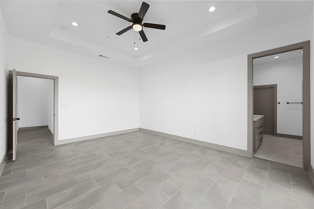 unfurnished bedroom with ensuite bathroom, ceiling fan, and a tray ceiling