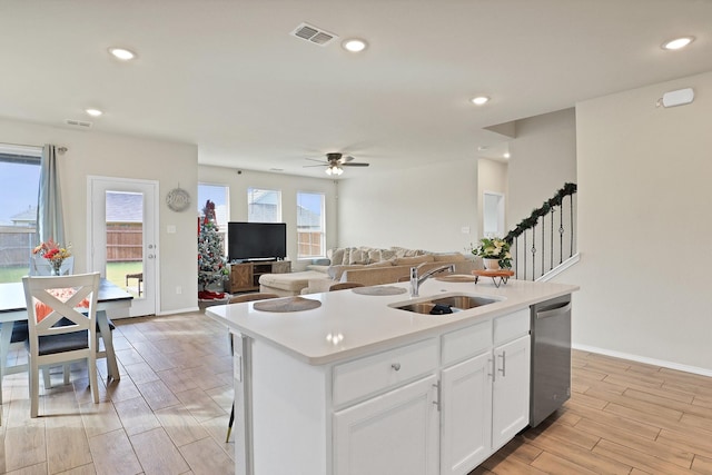 kitchen with stainless steel dishwasher, sink, a center island with sink, light hardwood / wood-style flooring, and white cabinets