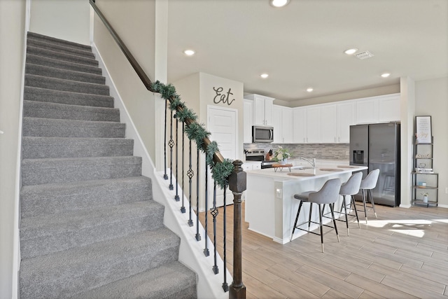 kitchen with a kitchen bar, stainless steel appliances, a center island with sink, light hardwood / wood-style flooring, and white cabinetry