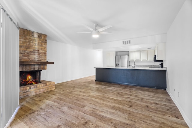 unfurnished living room featuring ceiling fan, sink, a fireplace, and light wood-type flooring