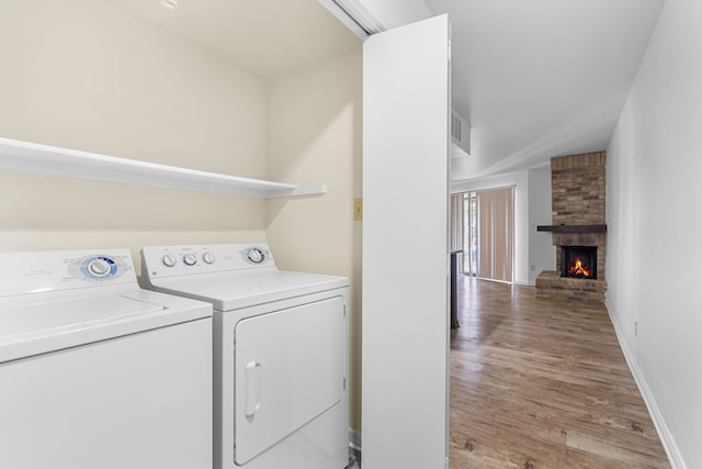 washroom with washing machine and dryer, wood-type flooring, and a fireplace