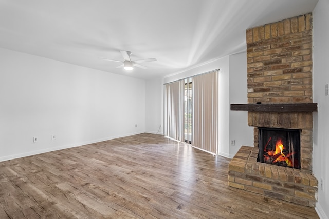 unfurnished living room with wood-type flooring, a brick fireplace, and ceiling fan