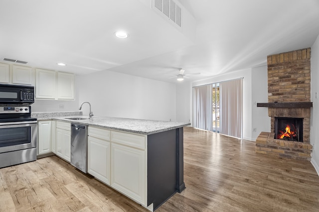 kitchen with ceiling fan, sink, a fireplace, appliances with stainless steel finishes, and light wood-type flooring