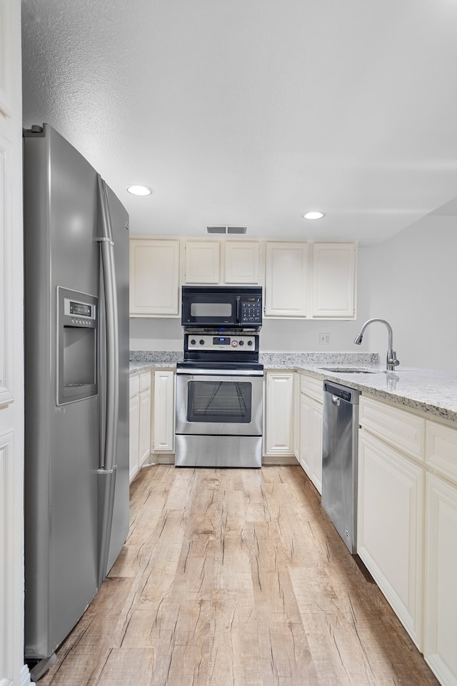 kitchen with light stone countertops, sink, light wood-type flooring, and appliances with stainless steel finishes