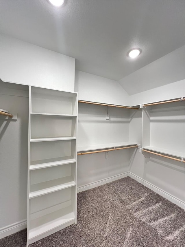 walk in closet with dark carpet and lofted ceiling