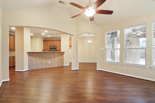 unfurnished living room featuring ceiling fan with notable chandelier, dark hardwood / wood-style floors, and vaulted ceiling