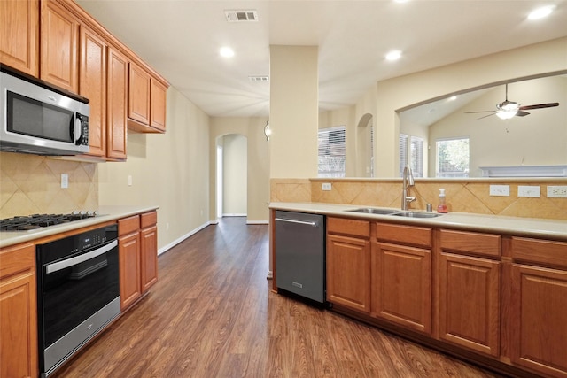 kitchen featuring decorative backsplash, appliances with stainless steel finishes, ceiling fan, dark wood-type flooring, and sink