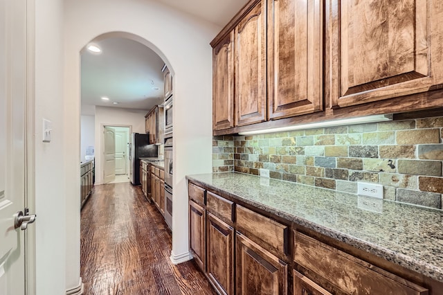 kitchen featuring decorative backsplash, light stone countertops, dark hardwood / wood-style flooring, and appliances with stainless steel finishes