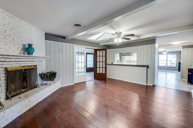 unfurnished living room with french doors, dark hardwood / wood-style flooring, a skylight, a brick fireplace, and beam ceiling