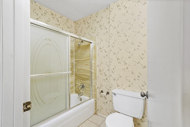 bathroom featuring tile patterned floors, toilet, combined bath / shower with glass door, and a textured ceiling