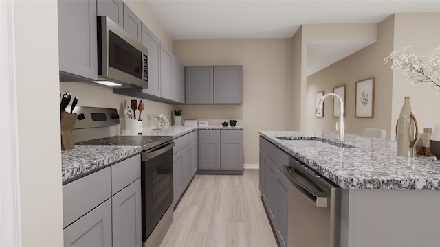 kitchen featuring gray cabinetry, sink, stainless steel appliances, an island with sink, and light hardwood / wood-style floors