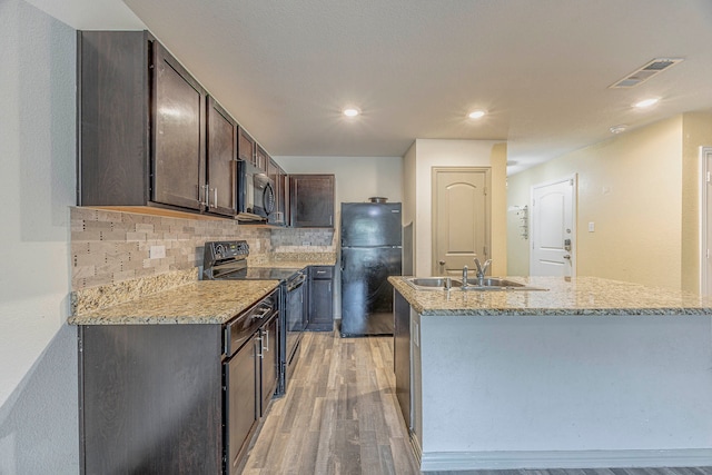 kitchen with light stone countertops, dark brown cabinets, sink, black appliances, and light hardwood / wood-style flooring