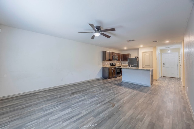 kitchen featuring backsplash, dark brown cabinetry, stainless steel appliances, a center island with sink, and light hardwood / wood-style flooring