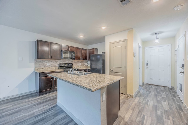 kitchen with a kitchen island with sink, black appliances, decorative backsplash, light hardwood / wood-style floors, and dark brown cabinetry