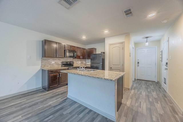 kitchen with dark brown cabinets, sink, black appliances, hardwood / wood-style flooring, and an island with sink