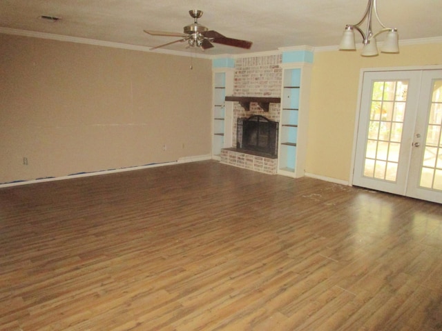 unfurnished living room with french doors, a brick fireplace, crown molding, hardwood / wood-style floors, and ceiling fan with notable chandelier