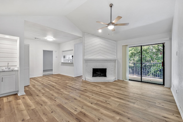 unfurnished living room featuring vaulted ceiling, sink, a brick fireplace, and light wood-type flooring