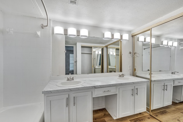 bathroom with vanity, tiled shower / bath combo, wood-type flooring, and a textured ceiling