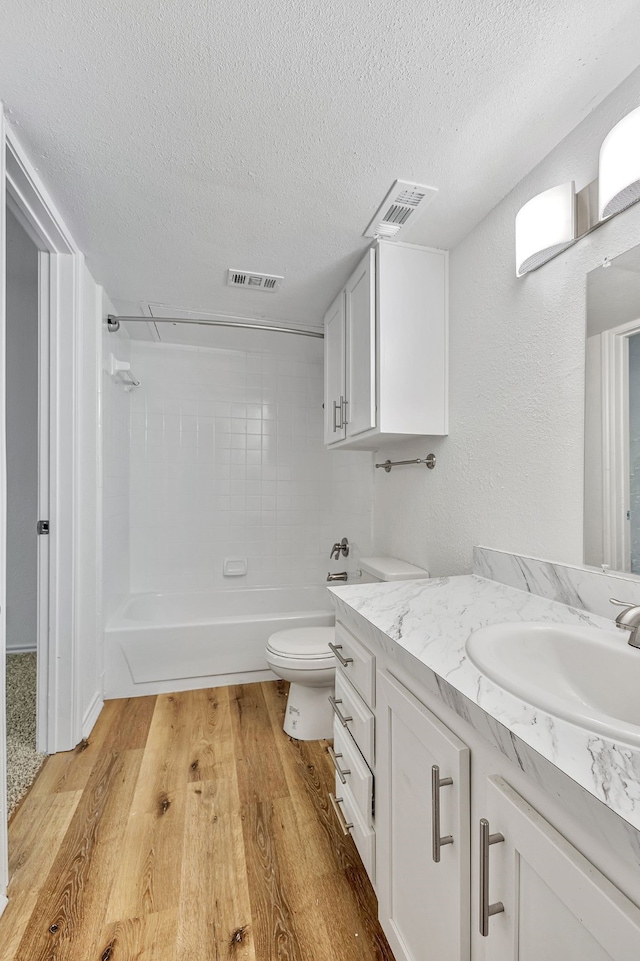 full bathroom with toilet, wood-type flooring, a textured ceiling, vanity, and tiled shower / bath combo