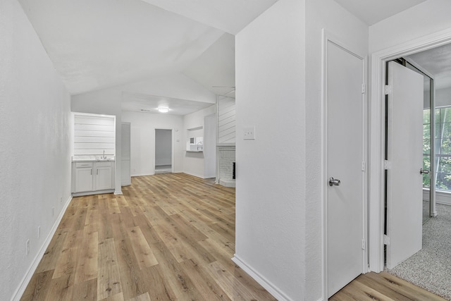 hall featuring lofted ceiling, sink, and light wood-type flooring