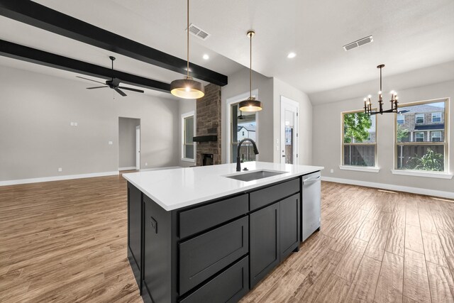 kitchen featuring sink, hanging light fixtures, light hardwood / wood-style flooring, stainless steel dishwasher, and an island with sink