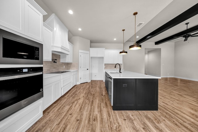 kitchen with sink, oven, white cabinets, and a center island with sink