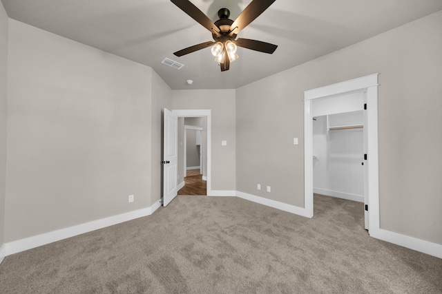 unfurnished bedroom featuring a spacious closet, light colored carpet, ceiling fan, and a closet