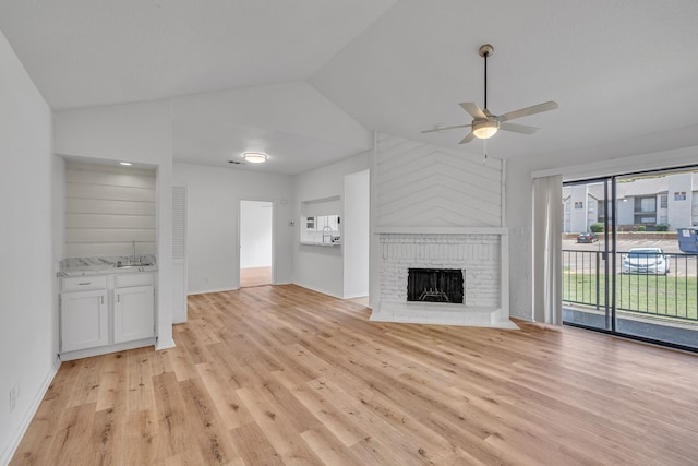 unfurnished living room with lofted ceiling, sink, a brick fireplace, light wood-type flooring, and ceiling fan