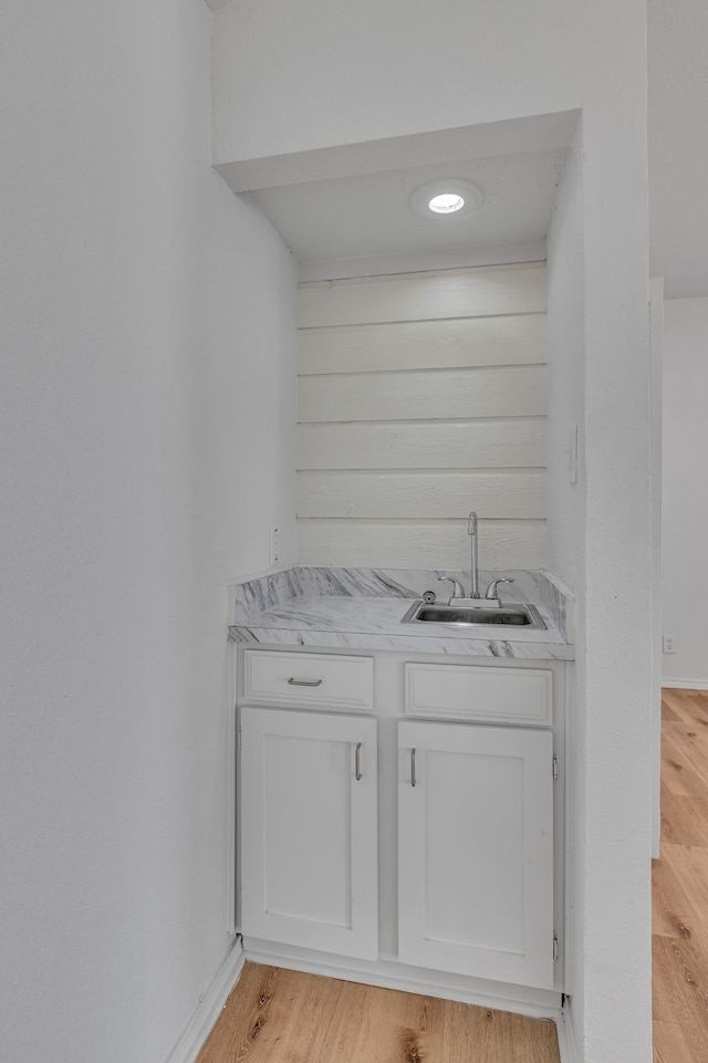 bar with white cabinetry, sink, and light wood-type flooring