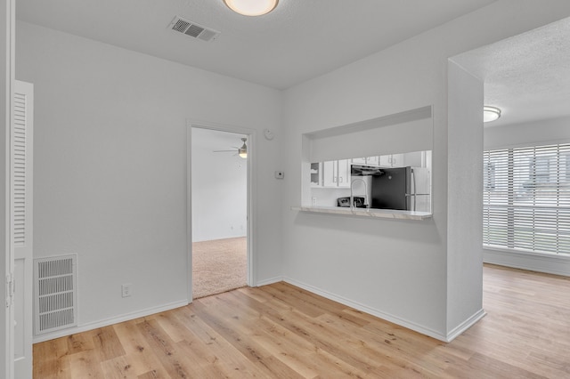 unfurnished living room featuring ceiling fan, light hardwood / wood-style flooring, and a textured ceiling