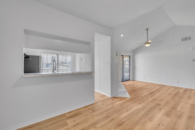 unfurnished living room with vaulted ceiling, sink, ceiling fan, and light wood-type flooring