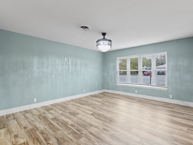 spare room featuring a chandelier and light wood-type flooring