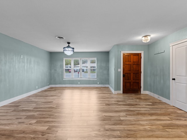 spare room featuring an inviting chandelier and light wood-type flooring