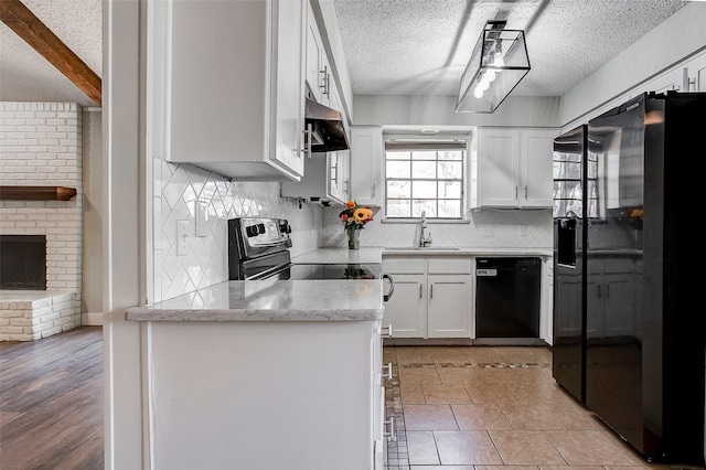 kitchen featuring black appliances, white cabinets, sink, light hardwood / wood-style flooring, and a fireplace