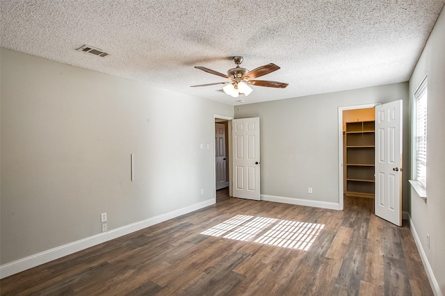 unfurnished bedroom featuring a textured ceiling, ceiling fan, a spacious closet, and dark wood-type flooring